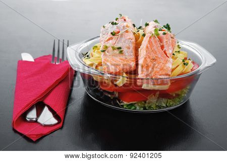 fresh fried natural pink salmon on italian traditional tagliatelle backed with tomato and vegetables served over black wooden table