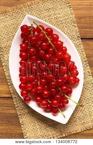 Raw red currants (lat. Ribes rubrum) on plate photographed overhead on dark wood with natural light