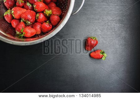 strawberries in a colander on a black desktop background