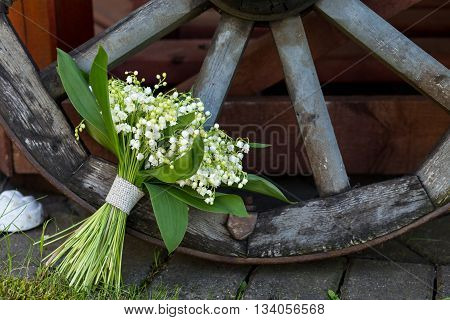 Summer bouquet of Lily of the valley flowers in the background of old decorative wooden wheel. Floral decoration. Floral arrangement.