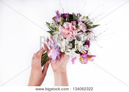 Hands holding a pastel bouquet from pink and purple gillyflowers on white background
