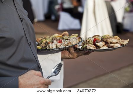 Waiter Carrying Plates Full Of Food At A Party. Hedonic Lifestyle.