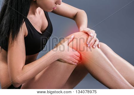 Body pain. Studio shot of beautiful young woman with dark brown hair. Woman suffering from knee pain. Red spot on knee