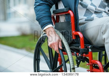 Adult man in wheelchair. Close up photo of male hand on wheel of wheelchair during walk