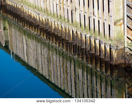 Wooden dock breakwall in a marina harbour with reflection in calm blue ocean sea