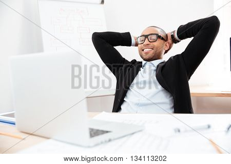 Successful relaxed young businessman sitting back in his chair with hands clasped behind his neck