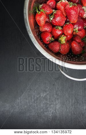 strawberries in a colander on a black desktop background