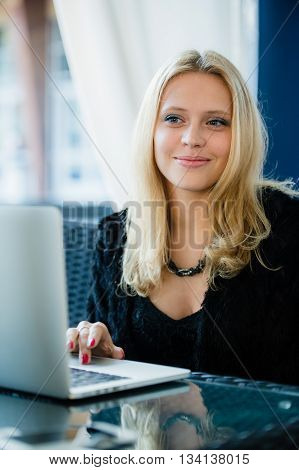 Young gorgeous European woman with pretty face thinking about something while sitting with laptop computer in cafe bar, dreamy beautiful female using portable net-book during work break in coffee shop