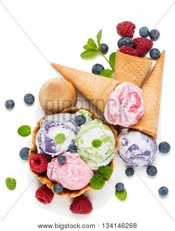 Top view of different scoops of ice cream with cones and raspberries and blueberries isolated on a white background.