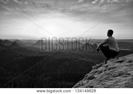 Adult In Black Trousers, Jacket Sit On Cliff's Edge