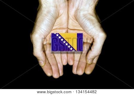 Flag of Bosnia and Herzegovina in hands isolated on black background.