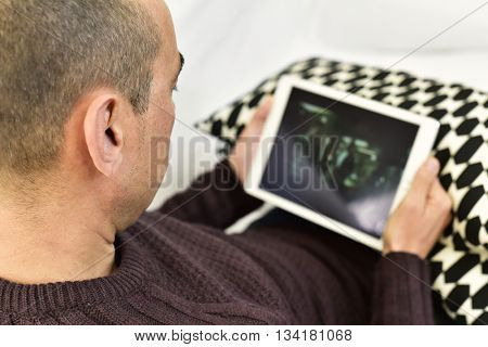 a young caucasian man lying on the couch watches a movie or a series in streaming in his tablet computer