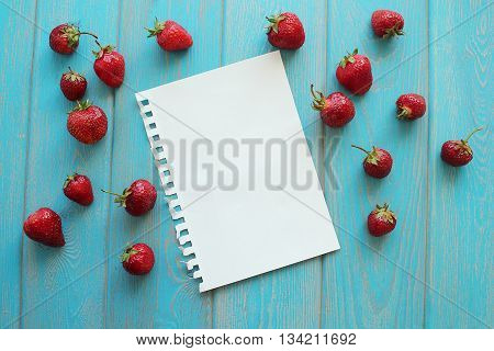 Strawberries on wooden grey desk with white paper sheet. Stock photo.