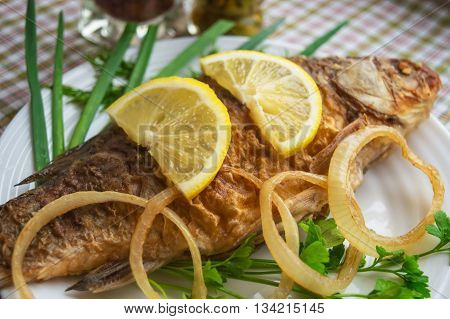 Roasted carp fish with greens on a white plate.