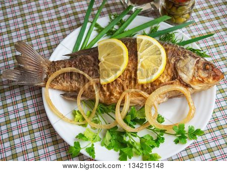 Roasted carp fish with greens on a white plate.