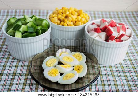 Many ingredients for the salad (sweet corn cucumber crab meat quail eggs) on a light background.