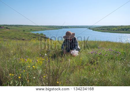 Woman in a straw hat gathers herbs in the prairies desert next to a large river. Wonderful sunny day. Azov steppes Ukraine.