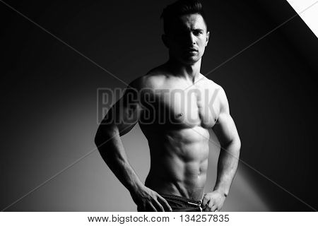 Sexy young man with muscular body and bare torso posing near window black and white