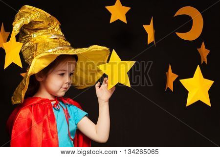 Beautiful five years old girl playing sky watcher with handmade stars and moon against black background