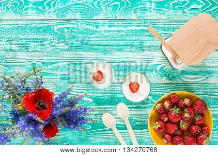 yogurt in glass jars strawberry sugar bowl flowers wooden spoons on turquoise colored wooden table top view