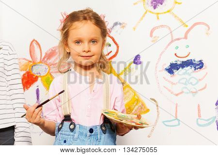 Cute smiling painter, five years old girl with brush and pallet drawing colorful picture