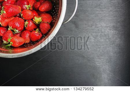 strawberries in a colander on a black desktop background