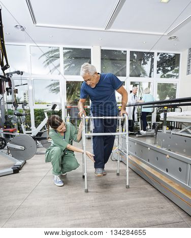 Female Nurse Assisting Senior Patient With Walker In Fitness Stu