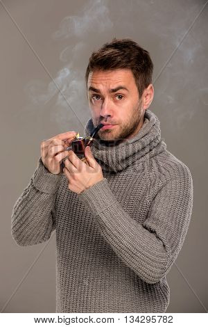 man lights a pipe with a match in the studio on a gray background
