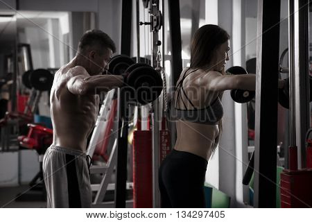 Young sexy athletic man and woman workout with dumbbells in gym. Perfect muscular body
