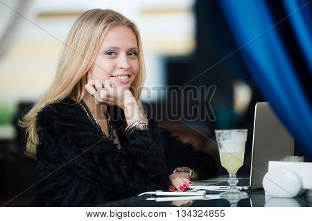 Young gorgeous European woman with pretty face thinking about something while sitting with laptop computer in cafe bar, dreamy beautiful female using portable net-book during work break in coffee shop.
