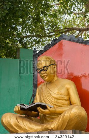 Chettinad India - October 17 2013: Golden statue of the actor and politician C.N Annadurai in the Karaikudi City. He reads a book and has black rimmed glasses. Green background.