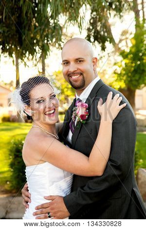 A bride and groom hold each other and laugh while looking at the camera. They are happy and posed but unposed at the same time.
