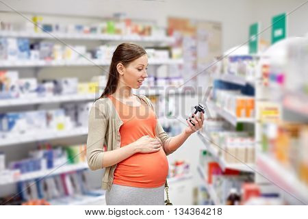 pregnancy, medicine, pharmaceutics, health care and people concept - happy pregnant woman reading label on medication jar at pharmacy
