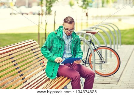 people, style, technology and lifestyle - happy young hipster man with tablet pc computer and fixie bike sitting on bench in city