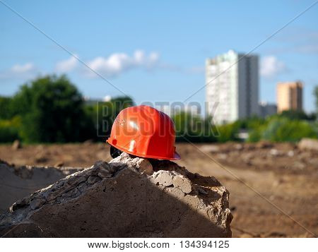 Orange helmet on a background of a vacant lot. A lot of sun. In the distance city high-rise buildings trees. Wasteland - a place under construction