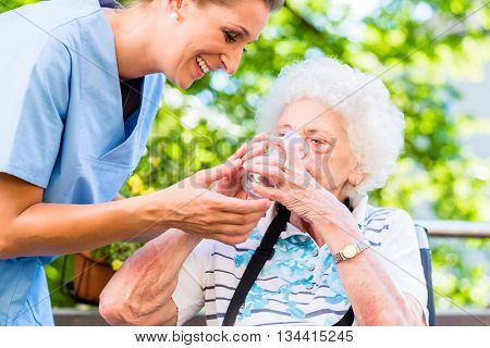 Geriatric nurse giving glass of water to senior woman
