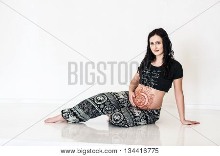 Pregnant young woman with mehendi tattoo on her belly sitting in the studio