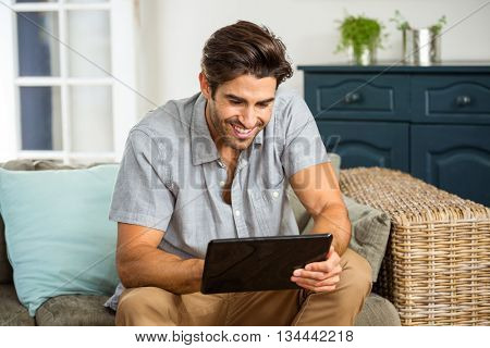 Young man sitting on sofa and using digital tablet in living room