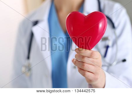 Female medicine doctor hands holding red toy heart in front of her chest closeup. Medical help cardiology care health prophylaxis prevention insurance surgery and resuscitation concept