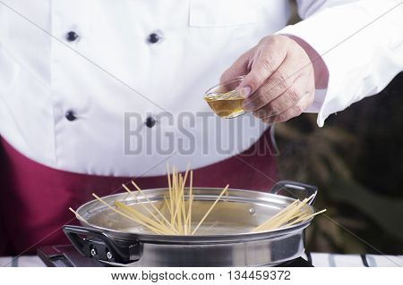 Chef pouring olive oil to spaghetti boiled in the pan / cooking spaghetti concept