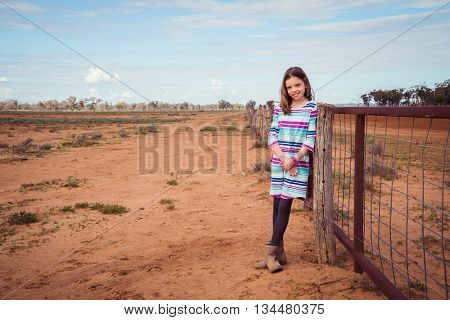 Young girl leaning on a fence in the dry drought ridden outback australia