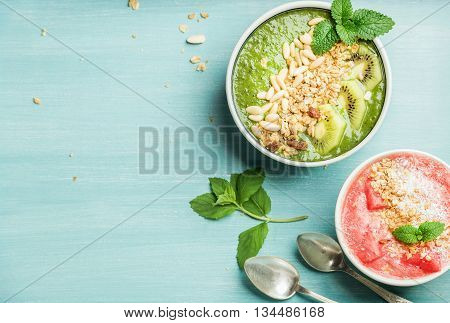 Healthy summer breakfast concept. Colorful fruit smoothie bowls with nuts and oat granola on turquoise blue background . Red and green, top view, copy space