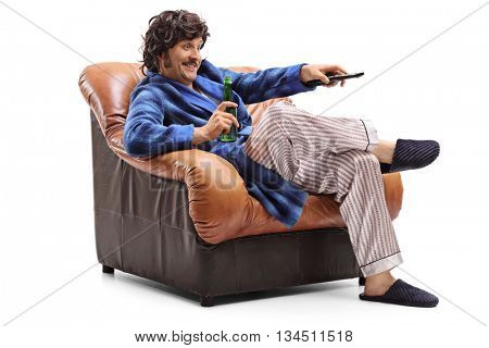 Young man sitting in an armchair with a beer in his hand and changing channels on TV isolated on white background