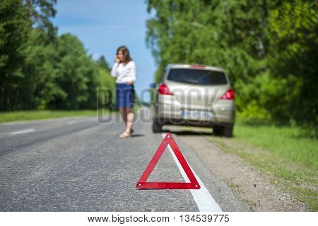 Red triangle warning sign female driver calling to a car assistance after breakdown. Focus on triangle.