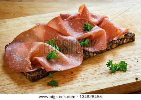 fine salami sausage slices and parsley garnish on a dark whole grain bread on a wooden kitchen board selected focus narrow depth of field
