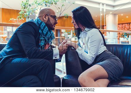 Arab man and the stylish girl sitting and holding hands in an airport lounge