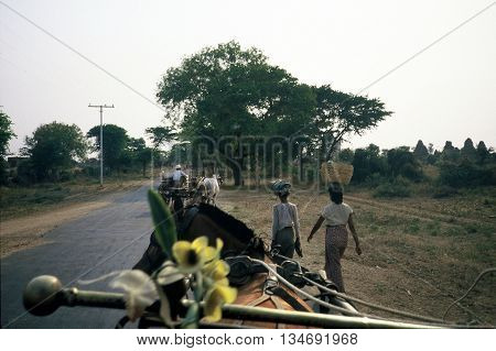 PAGAN / MYANMAR - CIRCA 1987: Two women carry bundles on their heads, while a man drives an oxcart.