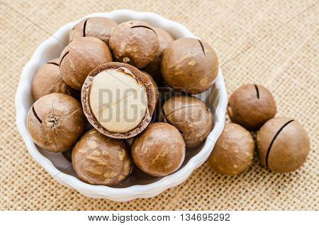 macadamia nuts in white bowl on sack background.