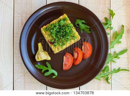 Central Asian traditional dish - pilaf (plov risotto) in the form of a square decorated with chopped parsley in clay bowl on a light wooden background. The top view