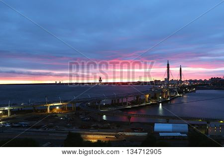 Colourful red and blue sunset above the river with long bridge in front. Industrial district of the city